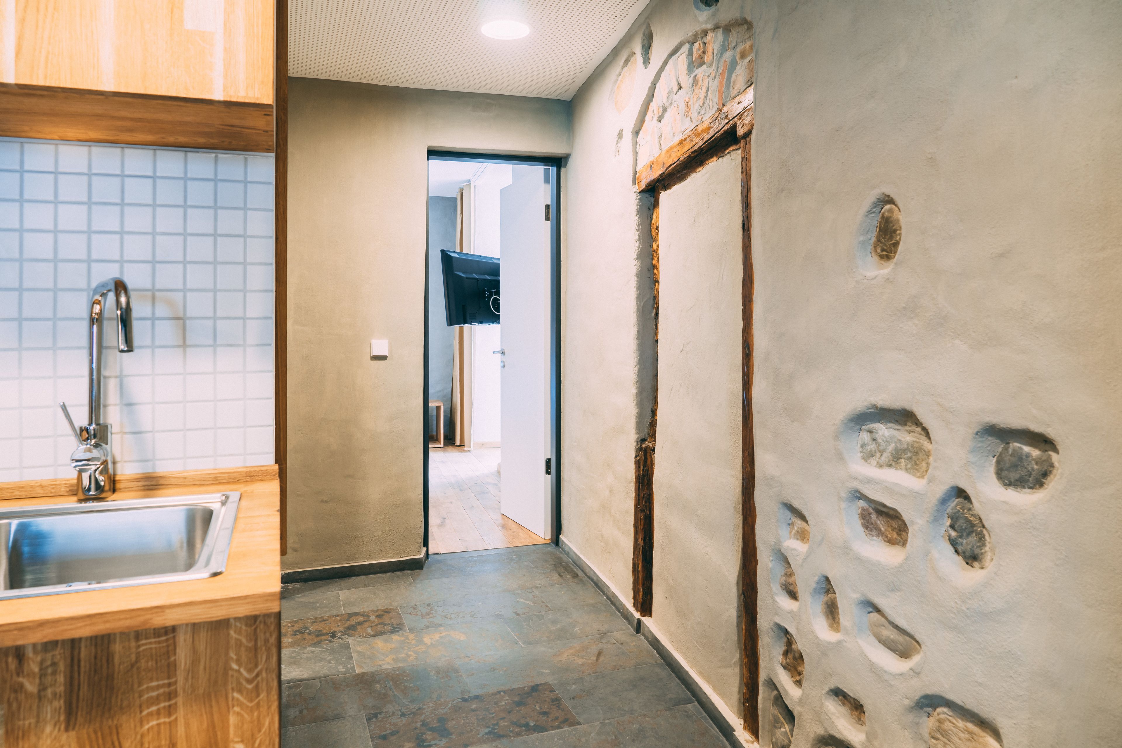 Un pasillo con pared de piedra, puerta de madera y salpicadero de azulejos en la zona de la cocina.