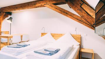 Una stanza con soffitto in legno, un letto con biancheria bianca, un piccolo tavolo in legno e una sedia.