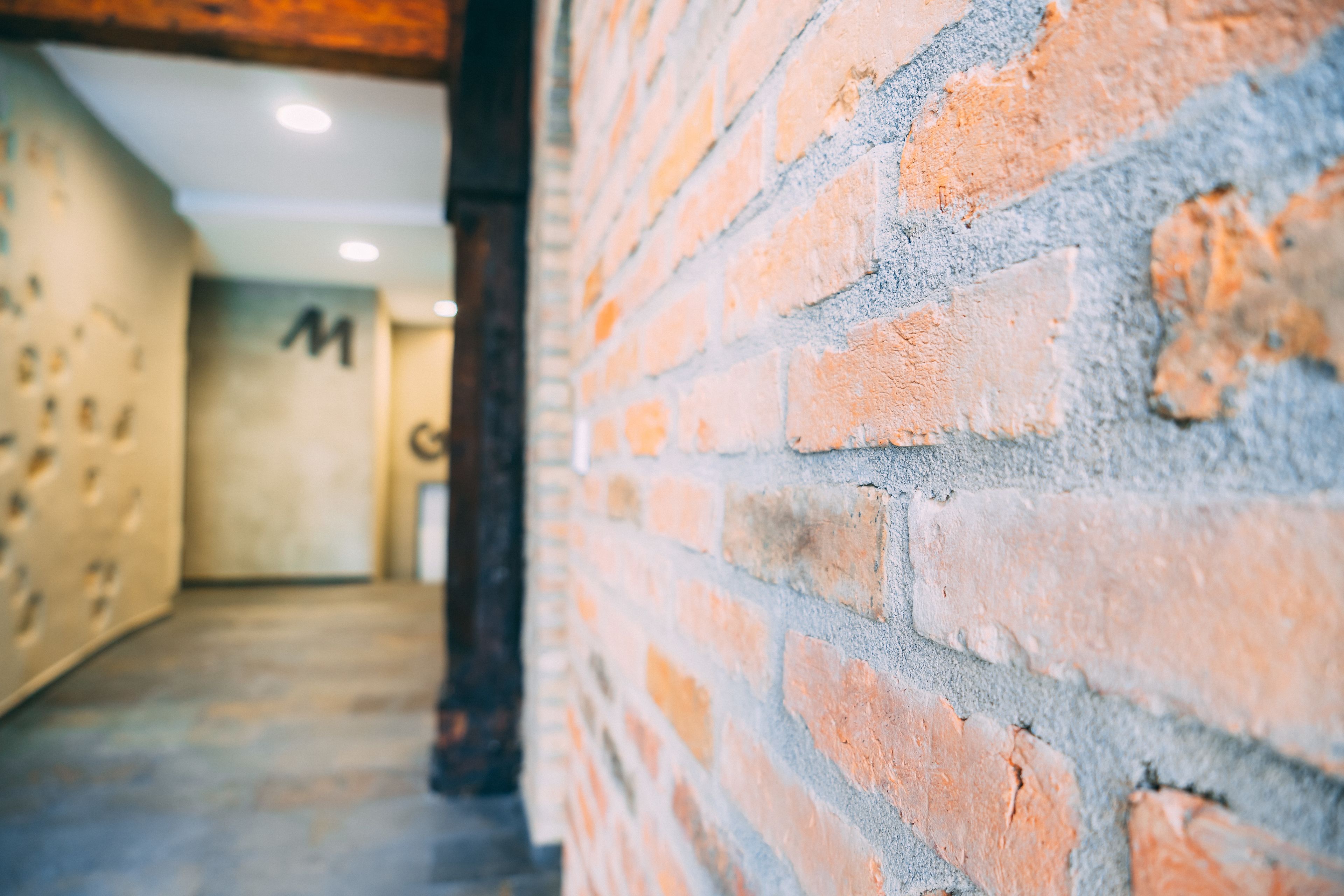 En tegelvägg med en delvis utsikt över en hall som leder till ett rum där bokstaven ”M” är målad på väggen.