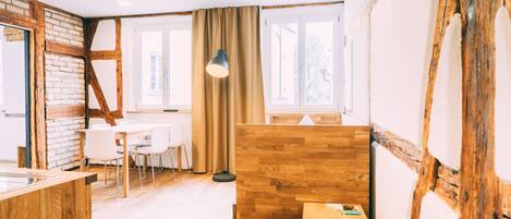 Una habitación con paredes de ladrillo visto, techo de madera, una mesa de comedor con sillas, una lámpara de pie y ventanas grandes con cortinas.