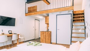 Una habitación de hotel moderna con zona de dormir elevada, un escritorio y una kitchenette.
