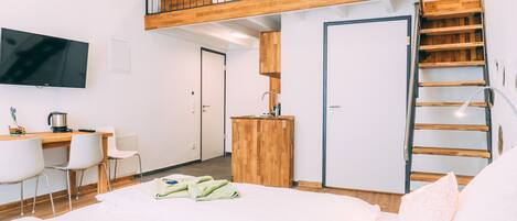 A modern hotel room with a lofted sleeping area, a desk, and a kitchenette.
