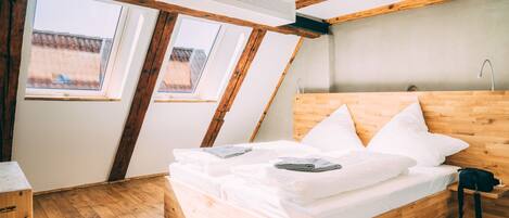 Una habitación con una cama de madera, dos ventanas y un techo inclinado.