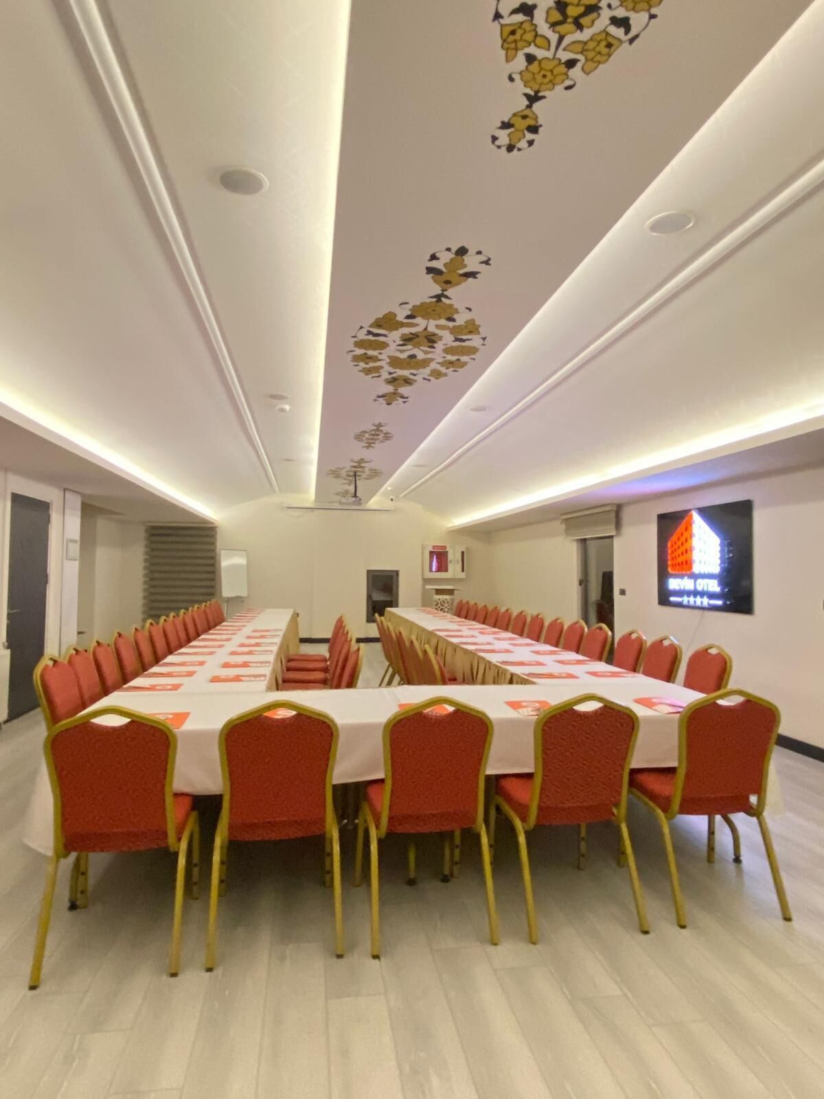 A conference room with a long table and red chairs, white walls, and a ceiling with floral patterns.