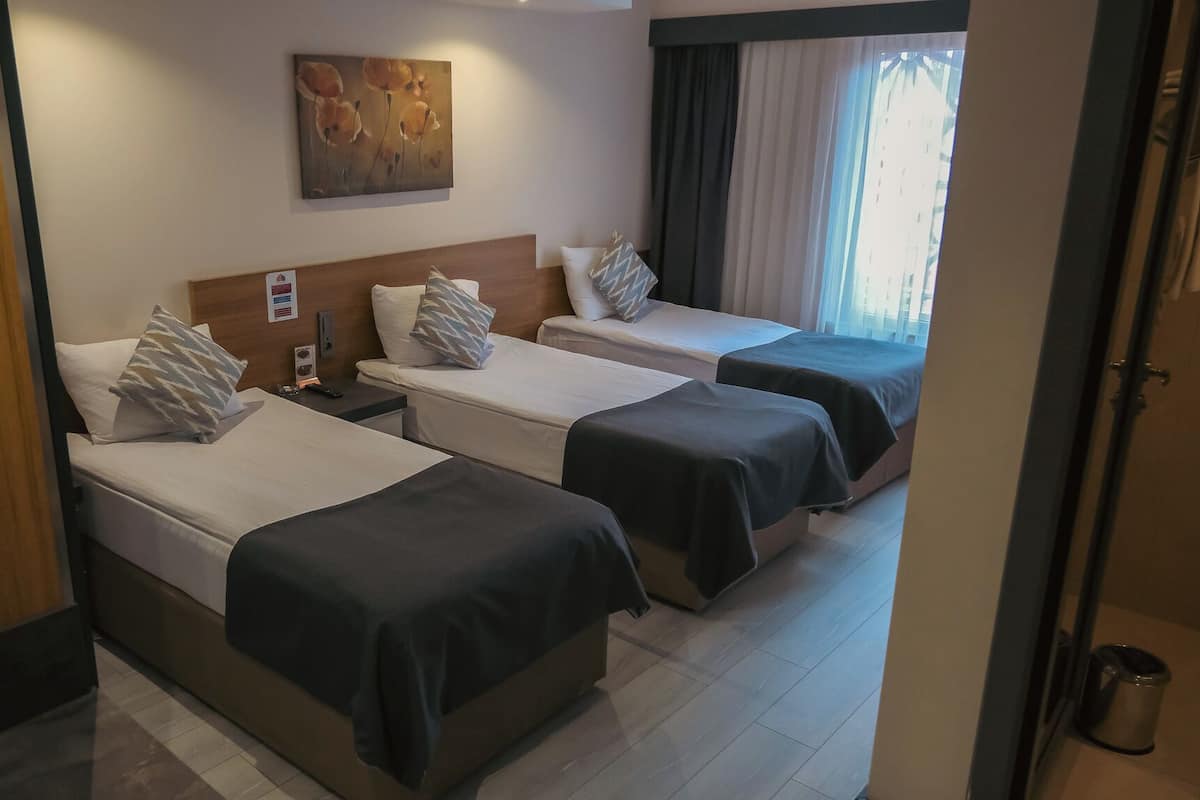 A hotel room with two beds, a wooden headboard, a painting on the wall, and a view of the outside through a window.