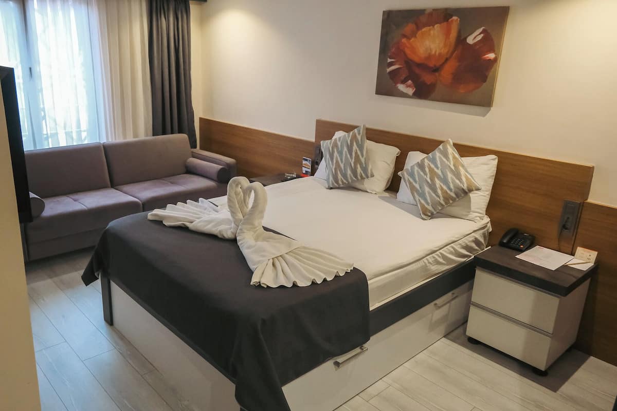 A hotel room with a bed, a nightstand, a desk, a sofa, and a painting on the wall.
