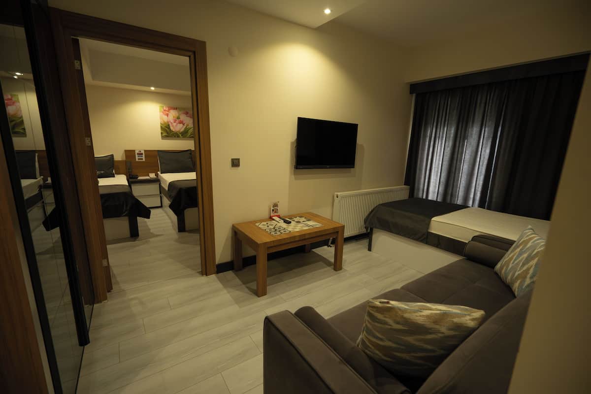 A modern living room with a sofa, a coffee table, a TV mounted on the wall, and a bed in the background.