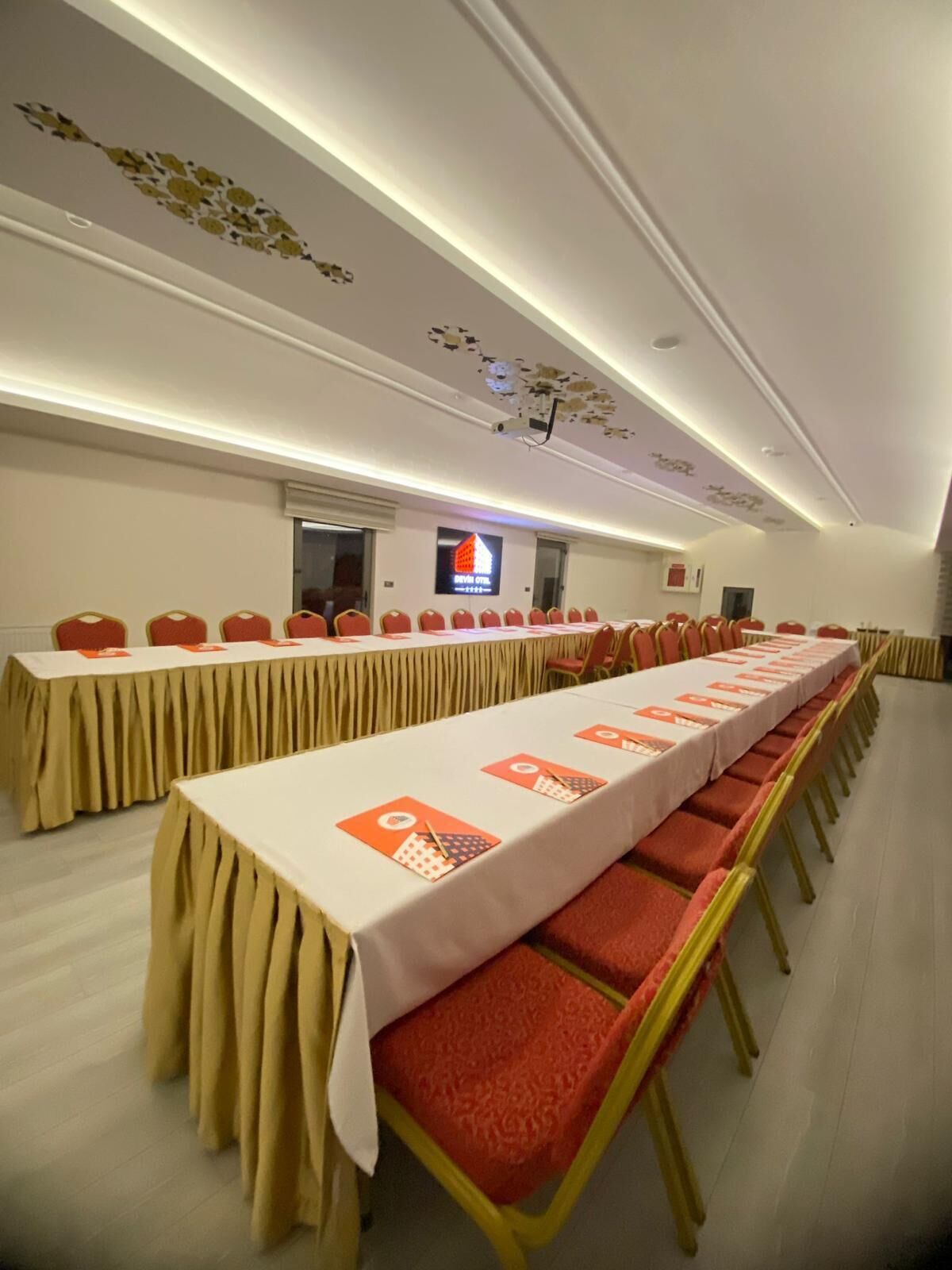 Una sala de conferencias con una larga mesa, sillas rojas y una pantalla de televisión en la pared.
