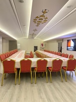 Una sala de conferencias con una larga mesa, sillas rojas y un techo decorado con motivos florales.