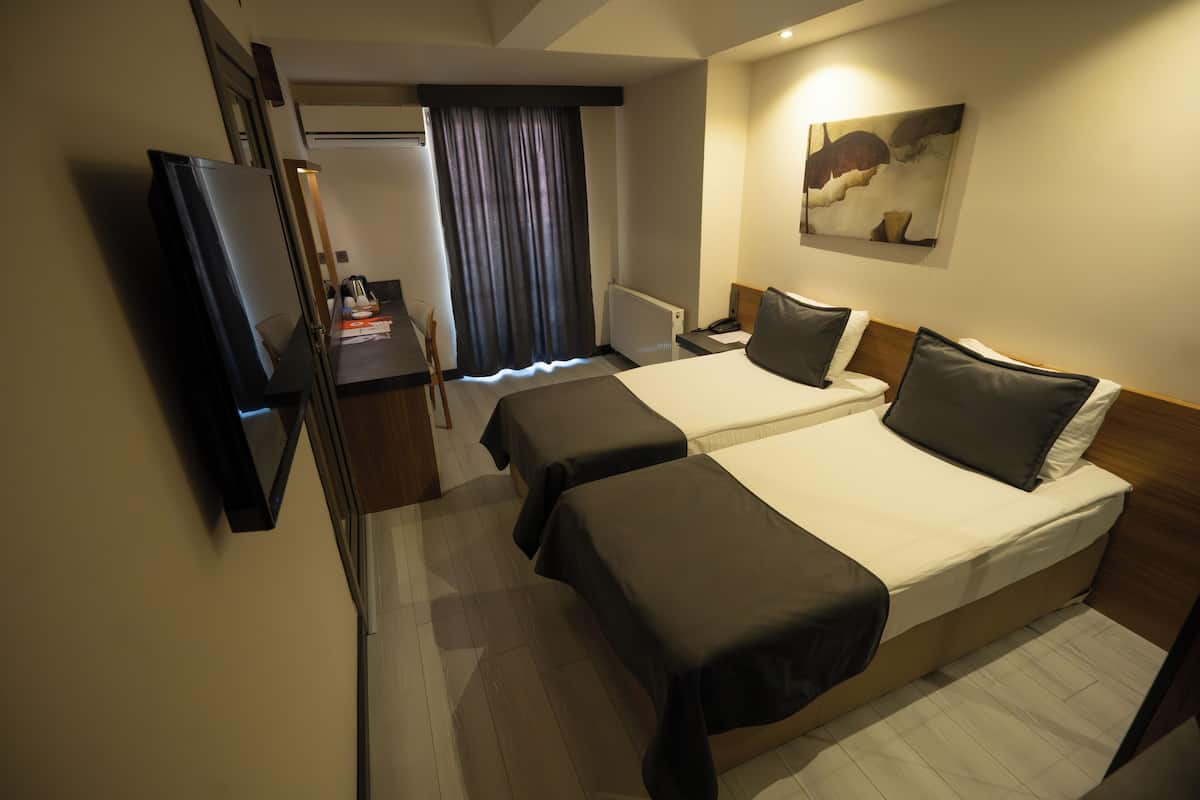 A hotel room with two beds, a TV, a desk, and a painting on the wall.