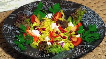 A plate of salad with various vegetables and cheese on a decorative plate, placed on a woven mat.