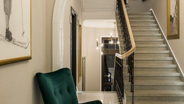 A staircase with a black railing, a green chair, and a table with a plant and a book. - Krupówki 17 Resort & Spa (Zakopane)
