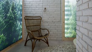 A wicker chair in a room with white brick walls and a large window overlooking a forest. - Krupówki 17 Resort & Spa (Zakopane)
