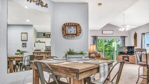 Ein Essbereich mit Holztisch und Stühlen, einem 'hello' Schild und einer Küche im Hintergrund.