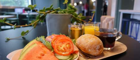 Bandeja de refeição com uma fatia de melancia, um sanduíche, uma xícara de chá e um copo de suco de laranja.