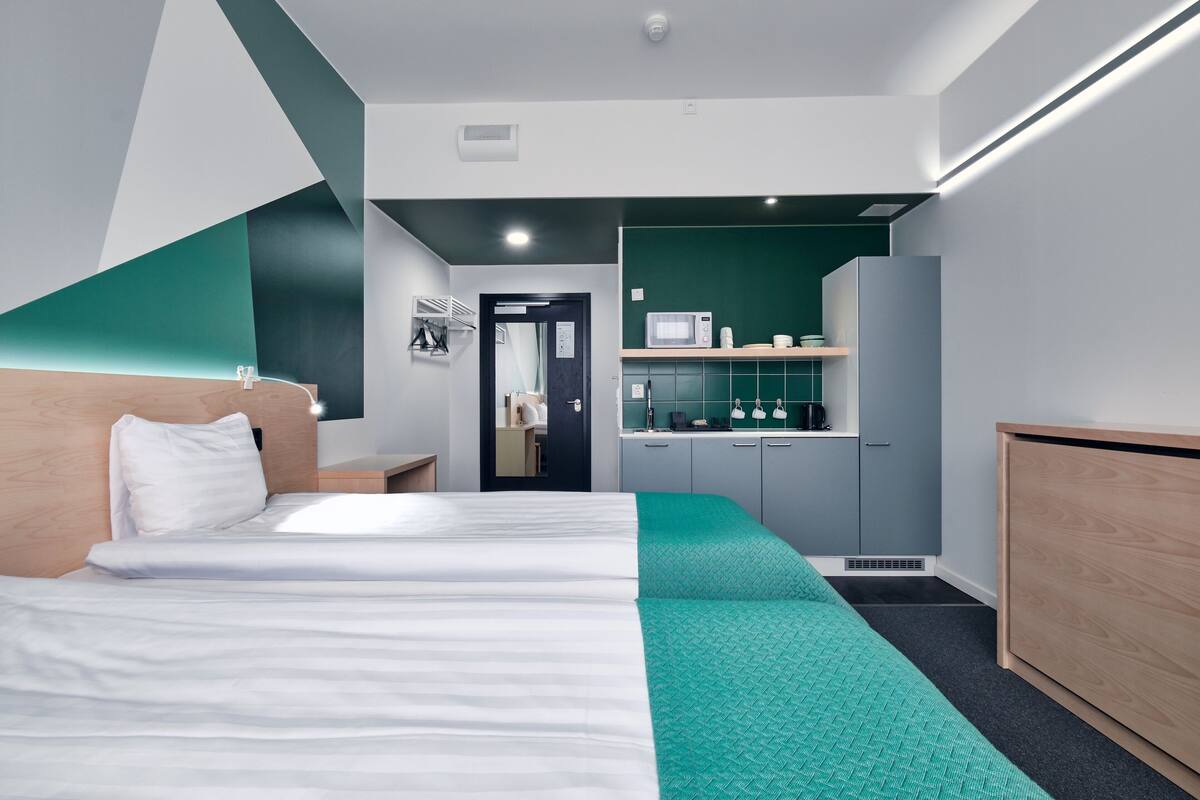 Une chambre d’hôtel moderne équipée d’un lit, d’un bureau, d’un four à micro-ondes et d’une petite kitchenette.