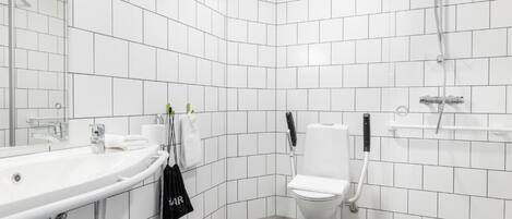 Un baño moderno con azulejos blancos, un lavabo blanco, un inodoro y una ducha.