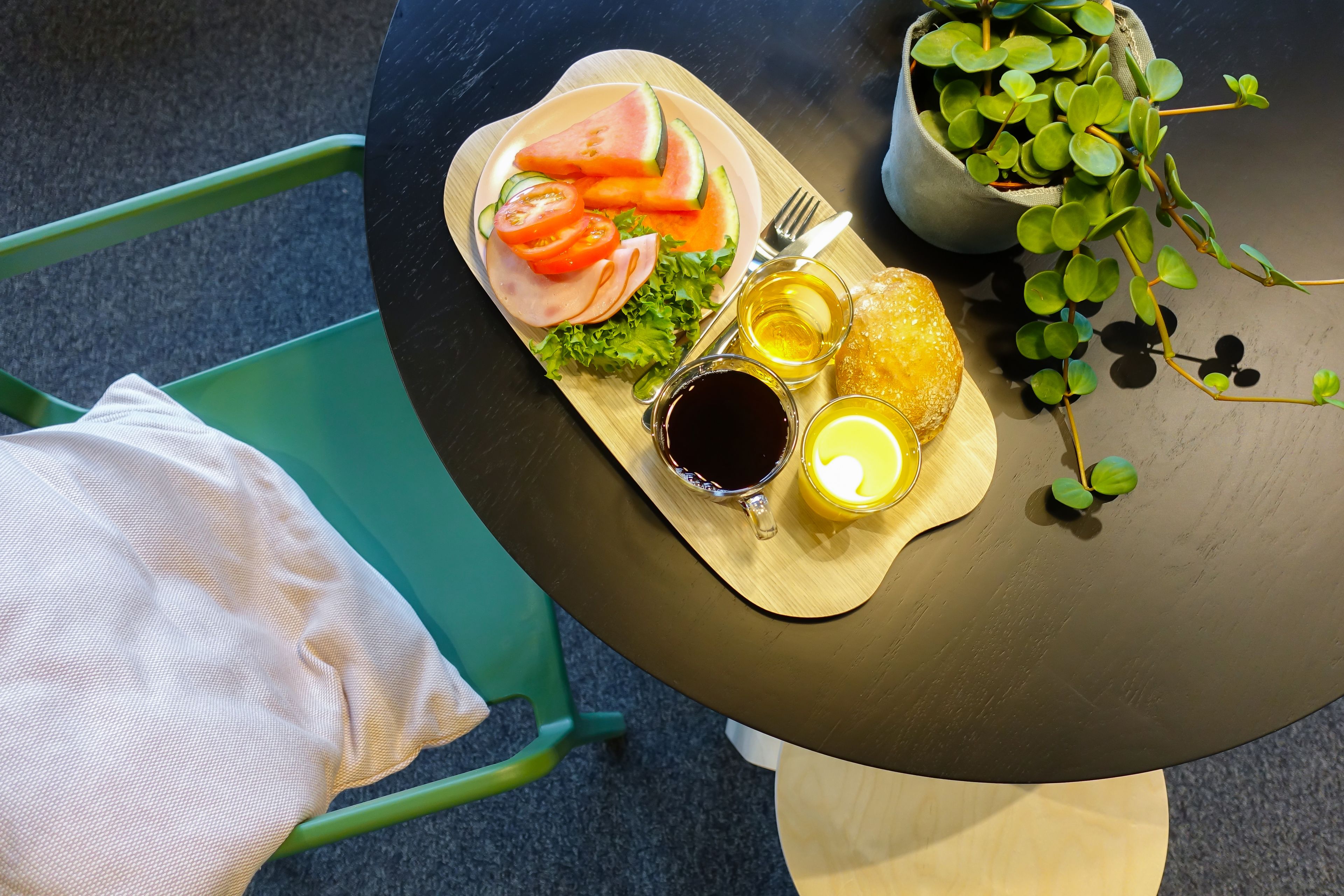 A meal tray with sliced watermelon, tomatoes, lettuce, and ham, accompanied by two drinks and a fork on a table.