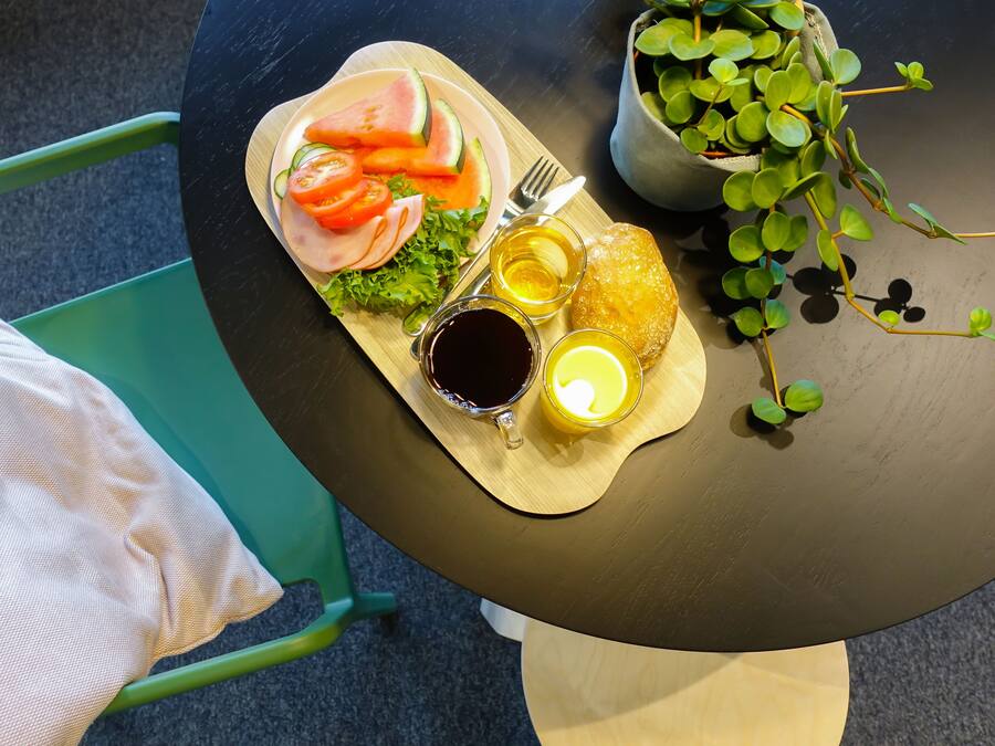 A meal tray with sliced watermelon, tomatoes, lettuce, and ham, accompanied by two drinks and a fork on a table.