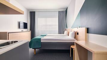 Moderni hotellihuone, jossa on sänky, työpöytä, televisio ja ikkuna, jossa on verhot.