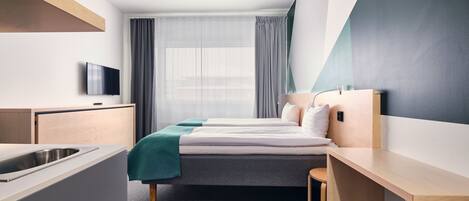 Una habitación de hotel moderna con cama, escritorio, televisor y ventana con cortinas.