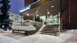 Een hotelentree met een bord waarop 'GREENSTAR HOTEL' staat, trappen die naar de ingang leiden, en sneeuw op de grond.