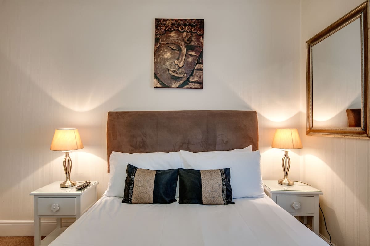 A hotel room with a large bed, two bedside tables with lamps, a wall-mounted artwork, and a mirror.