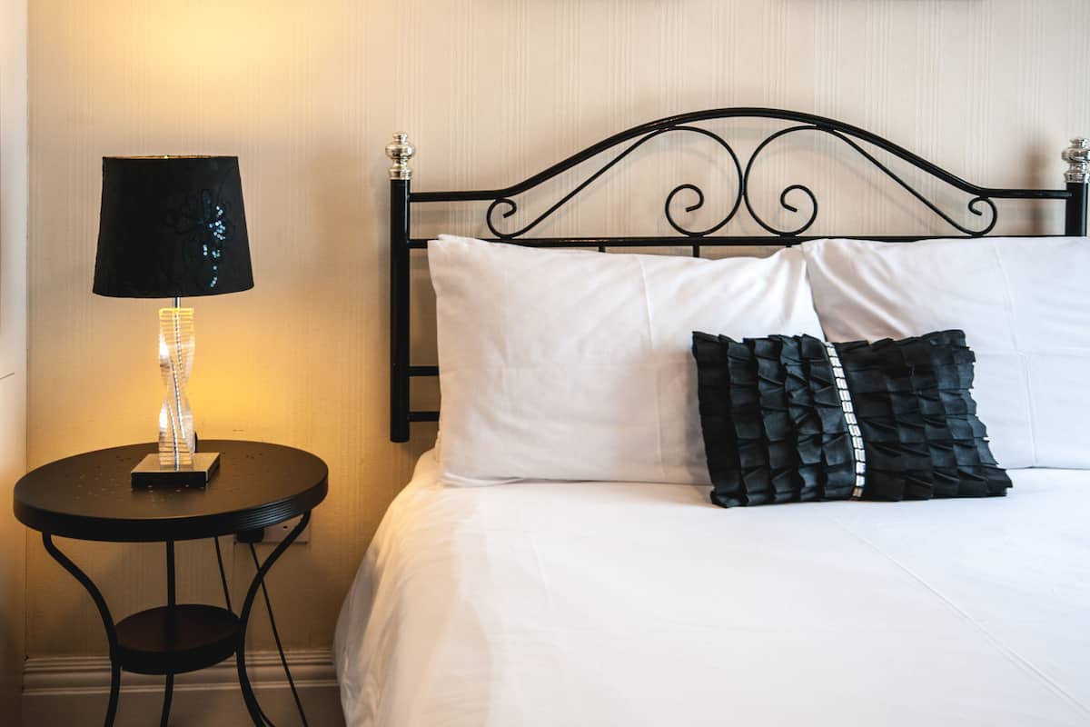 A neatly made bed with white and black pillows, a black metal headboard, and a small round table with a lamp beside it.