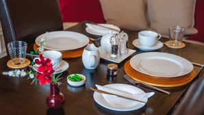 A dining table set with plates, cups, cutlery, and a vase with flowers. - Arlana Guest House (Cleethorpes)