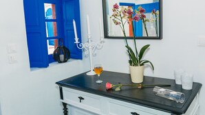 Una habitación con un aparador de madera oscura, un jarrón blanco con flores, un vaso de líquido ámbar y una puerta azul.