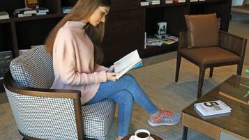Eine Person sitzt auf einem Stuhl mit Hunde-Zahn-Muster und liest ein Buch, mit einer Kaffeetasse auf einem kleinen Tisch in der Nähe.