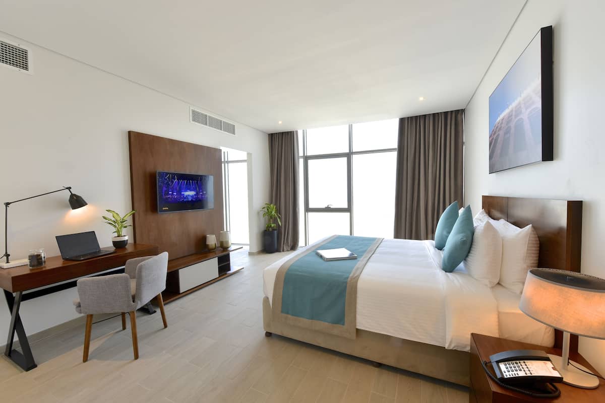 A modern hotel room with a bed, desk, chair, TV, and a phone.
