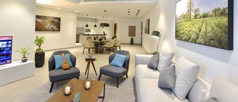 Una sala de estar moderna con un sofá, sillones, una mesa de centro con fruta, un tablero de ajedrez y un televisor.