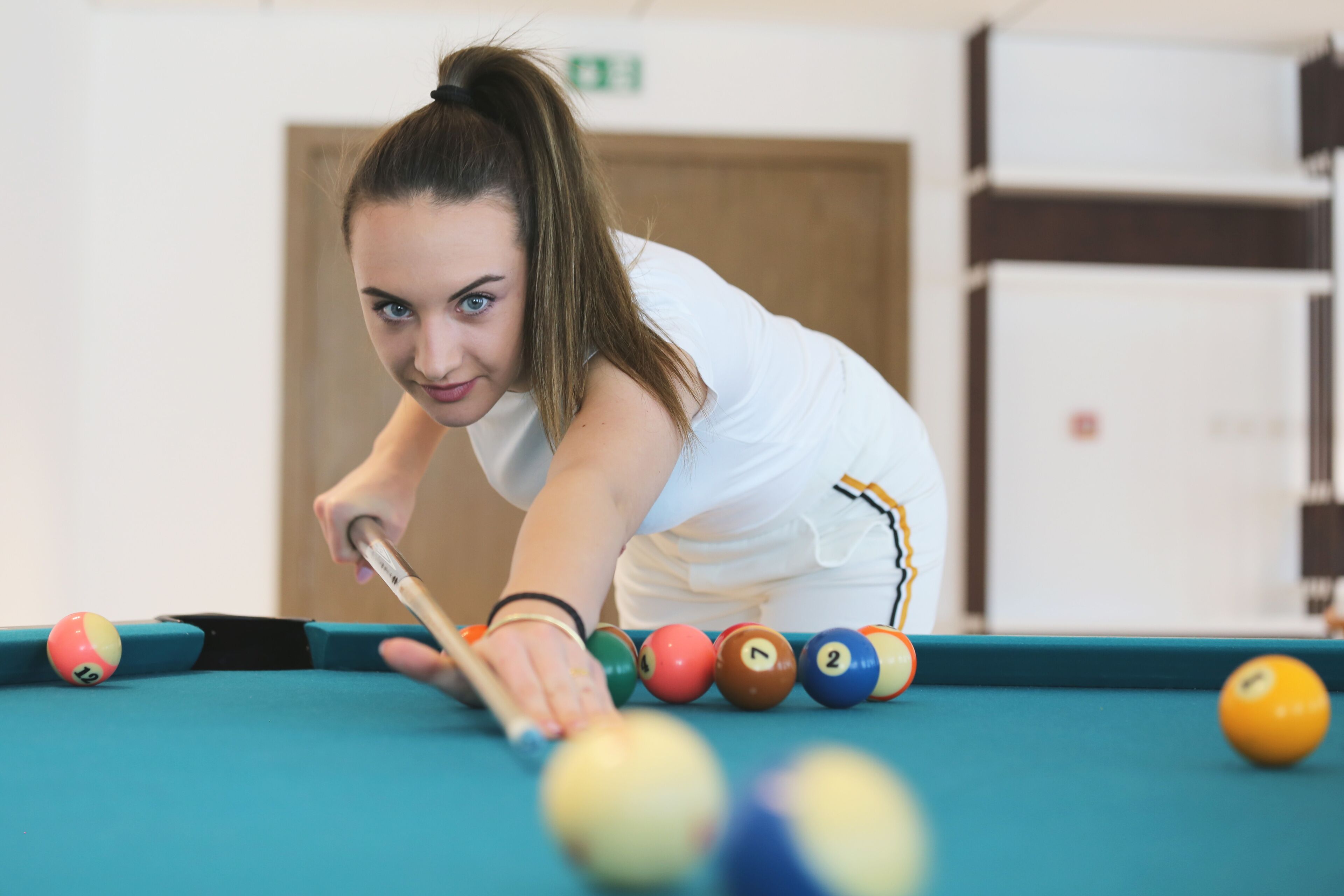 A person playing pool in a room with a green pool table and a white wall.