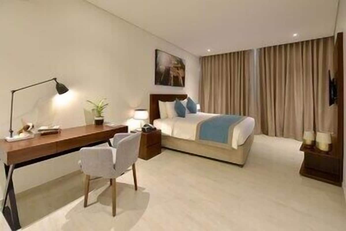 A hotel room with a bed, desk, chair, and a painting on the wall.