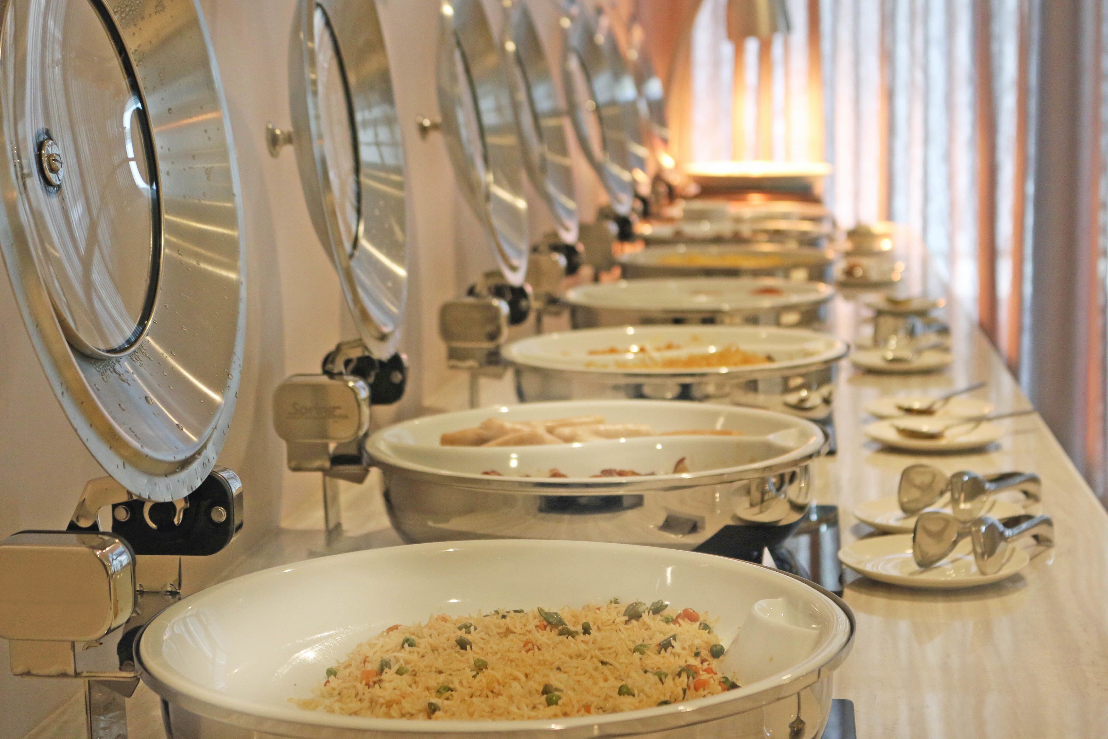A buffet line with multiple serving stations, each with a large bowl of food and a spoon.