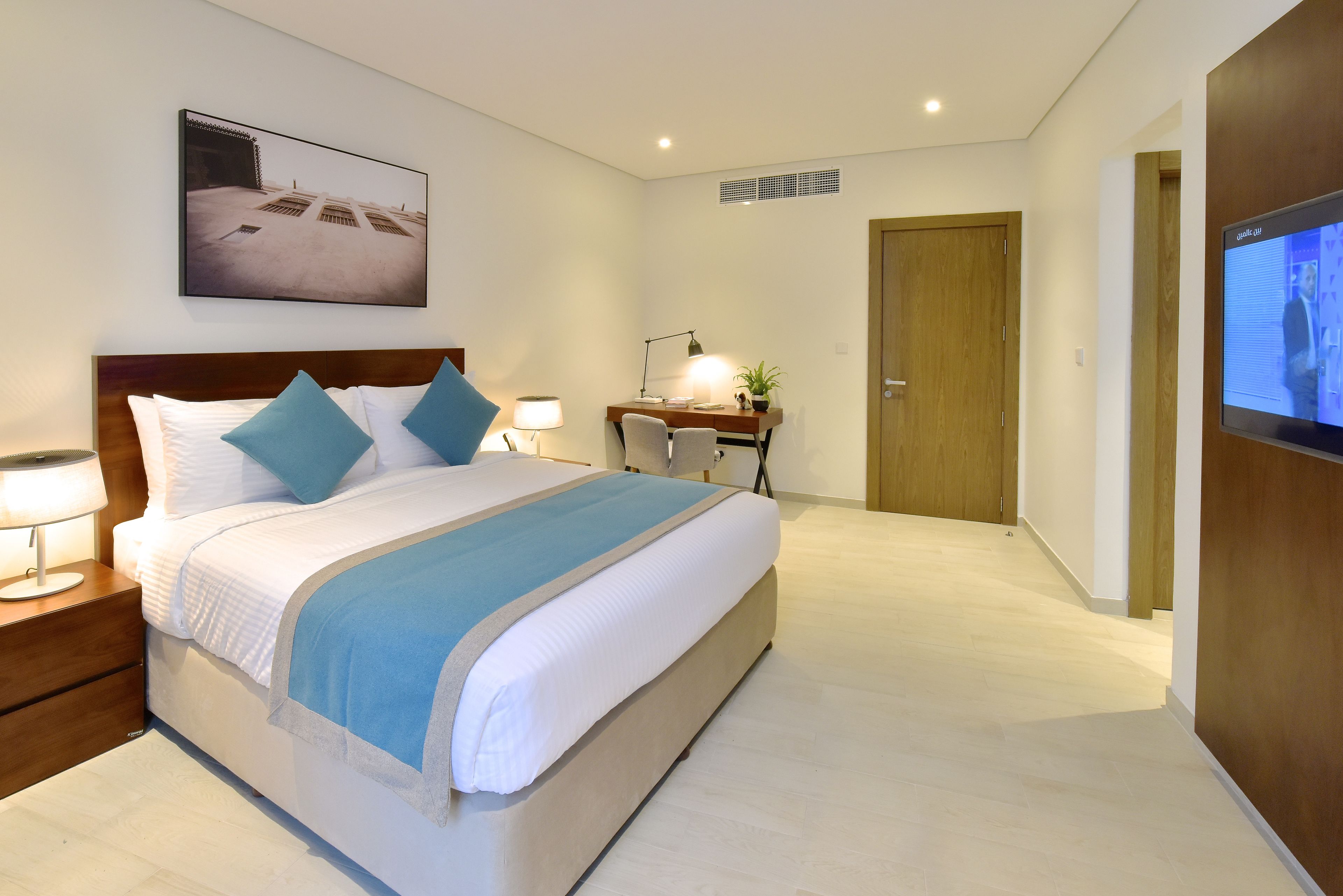 A modern hotel room with a large bed, bedside tables, a desk, and a television.