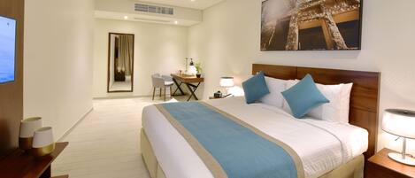 A hotel room with a large bed, a desk with a chair, a TV, and a painting on the wall.
