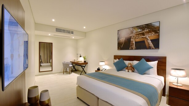 Ein Hotelzimmer mit einem großen Bett, einem Schreibtisch, einem Sessel, einem Fernseher und einem Bild an der Wand.