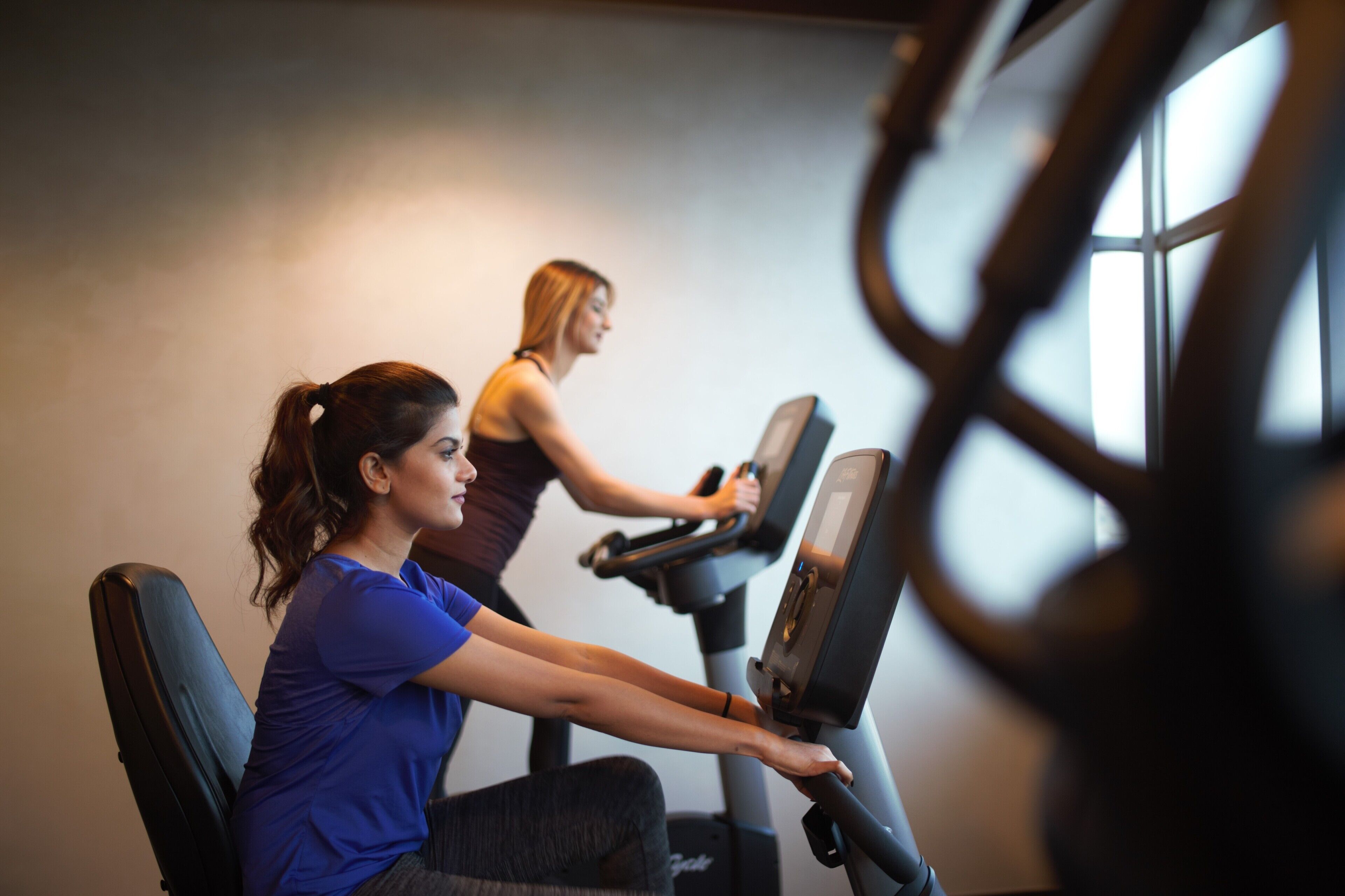 Two people using stationary bikes in a gym with a window in the background.
