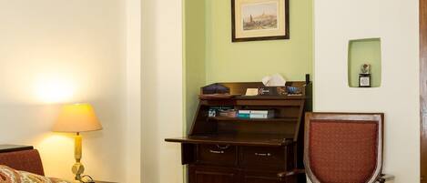 A hotel room with a bed, a desk, a chair, a lamp, and a framed picture on the wall.