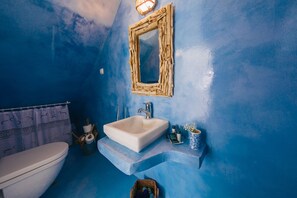 A bathroom with a blue wall, a white sink, a wooden-framed mirror, and a toilet. - GeoMare Beach House (Santorini)