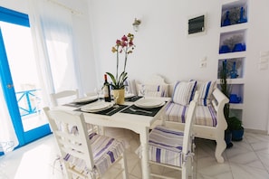 Un coin repas avec une table blanche dressée pour deux personnes, une orchidée en pot et un canapé rayé de bleu et de blanc.