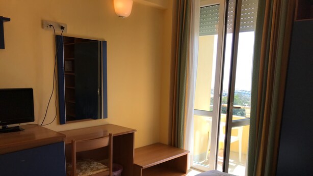 A bedroom with a bed, a desk, a chair, a TV, and a window with curtains. - Hotel San Carlo (Pietrasanta)