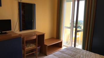 Ein Schlafzimmer mit einem Bett, einem Schreibtisch, einem Stuhl, einem Fernseher und einem Fenster mit Vorhängen.