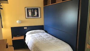 A single bed with a white duvet in a room with a yellow wall, a framed picture, and a bedside table with a lamp. - Hotel San Carlo (Pietrasanta)