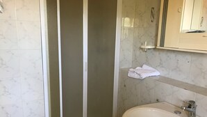 A bathroom with a white sink, a mirror, and a shower enclosure with frosted glass doors. - Hotel San Carlo (Pietrasanta)
