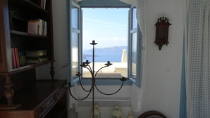 A room with a large open window, a bookshelf, a wall-mounted lamp, and a view of the sea. - 360 Blue (Santorini)