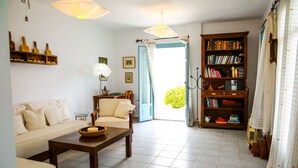 A living room with a sofa, coffee table, bookshelf, and a door leading outside. - 360 Blue (Santorini)