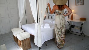 A bedroom with a four-poster bed, a bedside table with a lamp, and a small table with a box. - 360 Blue (Santorini)